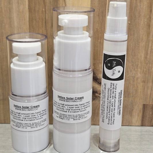 Three white pump bottles of Helios Solar Cream arranged horizontally on a wooden surface, with clear plastic caps visible.